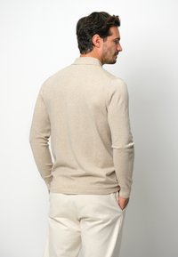 Beiger Langarm-Pullover aus weichem Material, mit klassischem Kragen und taillierter Passform, glatter Textur und minimaler Naht.