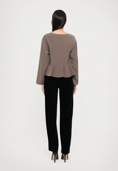 Brown long-sleeve top with a round neckline and drop shoulder design, paired with black velvet pants and high-heeled shoes.