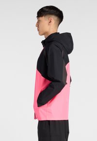 Veste imperméable noire et rose, dotée d'une capuche, de poches latérales et d'un design coloré. Fabriquée en tissu léger et lisse.