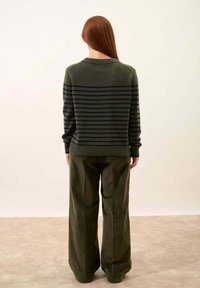 Zielony sweter z dzianiny z granatowymi poziomymi paskami, z prążkowanym dekoltem i dołem, zestawiony z szerokimi, oliwkowymi spodniami. Miękka tekstura.