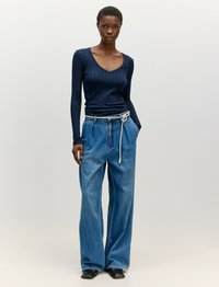 Marineblaue, langärmlige Ripp-Top kombiniert mit hochtaillierten, weiten Jeans aus Denim. Die Jeans haben einen Zugbandgürtel und eine entspannte Passform. Schwarze Schuhe runden das Outfit ab.