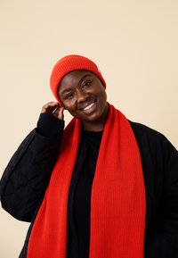 Red ribbed beanie and matching scarf made of warm knit fabric, paired with a black quilted jacket. Simple and functional design.