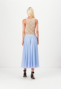 Beige strikket tanktop med teksturdetaljer, parret med en lys blå tulle maxiskørt og sorte højhælede sko med ankelremme.