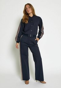 Navy track jacket with cropped design, button closure, and striped sleeves. Paired with matching wide-leg pants featuring side stripes.