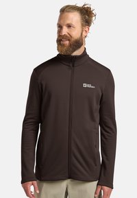 Veste en polaire brune à fermeture éclair avec un col haut, une surface texturée et des poches latérales. Présente un logo sur la poitrine gauche. Tissu durable.