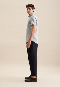 Camicia azzurro chiaro a maniche corte con colletto a punte, abbinata a pantaloni neri slim-fit e scarpe nere stringate. Tessuto dalla consistenza liscia.