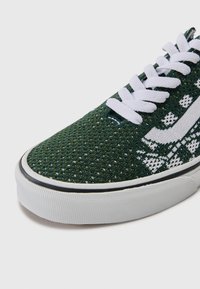 Grønne strikkede sneakers med hvide snørebånd og dekorativt hvidt mønster. Har en tekstureret gummisål og kontrasterende sort kant.