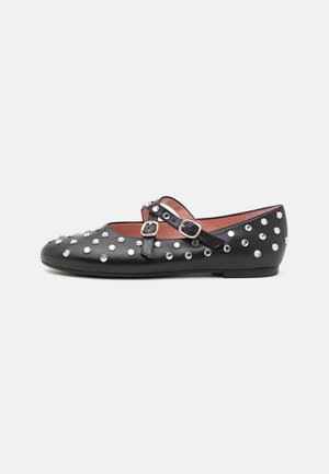 Zwarte platte schoen met twee verstelbare riempjes met gespsluiting en zilveren ronde studs die het oppervlak bedekken, zijaanzicht.