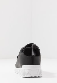 Černé tenisky s hladkým koženým svrškem, které mají bílou strukturovanou podrážku. Na zadní straně je vystlaná poutko pro snadné obouvání a detaily s logem.