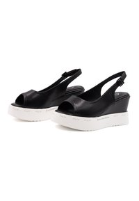 Sandali con tacco a cuneo neri in pelle, con punta aperta e una piattaforma bianca texturizzata che presenta la scritta del marchio sul lato.