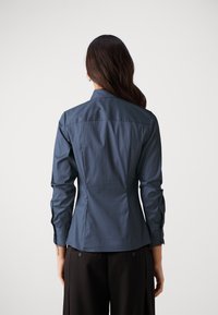 Camicia aderente blu navy con maniche lunghe e colletto a punta. Tessuto liscio con dettaglio del dorsale e polsini con bottone.