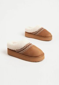 Barna velúr slip-on papucsok, bolyhos fehér béléssel, hullámos mintával és vastag talppal a kényelem érdekében. A texturált anyag javítja a tapadást.