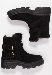Botas de ante negras hasta la mitad de la pantorrilla, con doble hebilla, forro de piel suave y suela de goma negra resistente con surcos profundos.