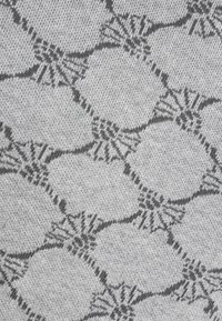 Tessuto in tessile con una base grigio chiaro e un motivo geometrico grigio scuro che ricorda forme sovrapposte con dettagli intricati.