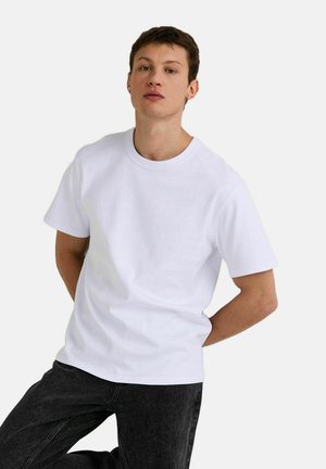 T-shirt en coton blanc à manches courtes et col rond, associé à un jean en denim foncé. Design simple, texture lisse et coupe classique.