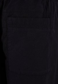 Sorte stofshorts med en baglomme med synlig syning. Materialet er glat med en let tekstureret overflade.