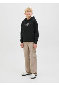 Svart huvtröja med ficka fram, beige cargobyxor med sidfickor och svart-vita sneakers. Neutral bakgrund.