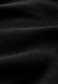 Tissu noir doux avec des plis subtils et une texture fine en maille, créant de doux jeux d'ombres et de lumières.