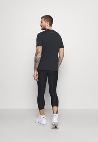 Sort t-shirt med korte ærmer og sorte leggings lavet af strækbart materiale, båret med hvide sneakers. Har tatoveringer på den synlige arm.