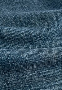 Gros plan d'un tissu denim bleu texturé montrant les fils tissés et des plis subtils.