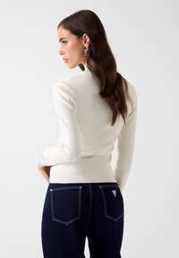 Witte gebreide trui met een hoge hals, lange mouwen en een aansluitend model. Gecombineerd met donkerblauwe jeans met contrasterende stiksels en een logo.