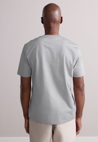 Szürke pamut rövid ujjú póló, kerek nyakkal és sima textúrával. A hátsó nézet laza szabást és egyszerű kialakítást mutat.