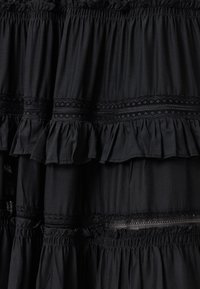 Robe noire à couches avec des ourlets à volants et des détails en dentelle complexes entre les couches, avec une texture lisse et fluide et une taille élastiquée.