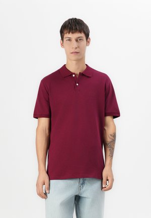 Polo en coton de couleur bordeaux, avec un col classique, trois boutons et un petit logo. Assorti à un jean bleu clair.