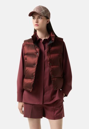 Maroon puffer vest with horizontal stitching and press studs, worn over a matching shirt and shorts. Cap features a geometric pattern.