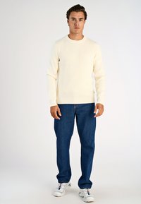 Cremefarbener gerippter Pullover, blaue Jeans und weiße Sneakers. Schlichtes Design mit langen Ärmeln und rundem Halsausschnitt.
