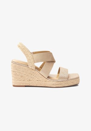 Sandale compensée avec des bretelles élastiques croisées, dessus en tissu beige, plateforme en espadrille texturée et semelle lisse couleur brun clair.