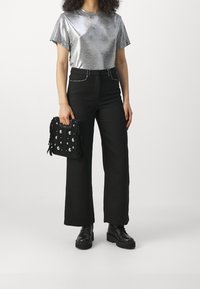 T-shirt métallique argentée à manches courtes, pantalon noir taille haute, sac à main noir à franges avec clous, et bottes noires à semelles épaisses.