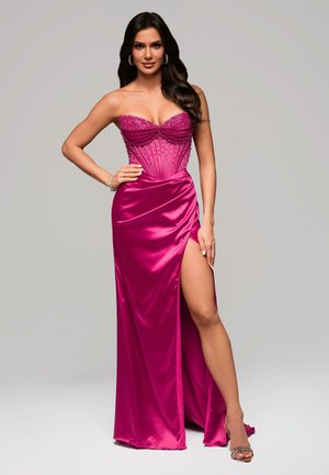 Abito fucsia senza spalline con corpetto decorato, design arricciato e spacco alto; texture in satin liscio; dettagli argentati e tacchi visibili.