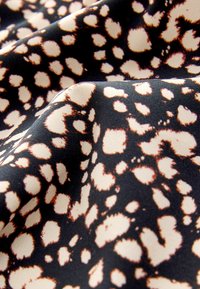 Svart tyg med ett leopardmönster som har stora beiga fläckar omgivna av mörkbrunt, med en slät textur och matt yta.