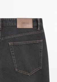 Jean en denim foncé avec une étiquette en cuir marron à la taille, des coutures contrastées et une poche arrière.