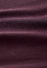 Tessuto di un profondo bordeaux con una superficie liscia, caratterizzato da un leggero lucido e pieghe ripiegate, che mostra un motivo di tessitura uniforme.