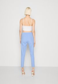 Light blue tailored pants with a smooth texture, featuring a fitted waistband and tapered legs. Worn with a white cropped top and strappy heels.