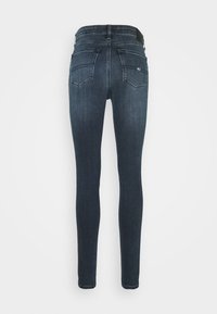 Mörkblå tajta jeans med bakfickor, bälteshällor och en liten logotyp på höger bakficka.