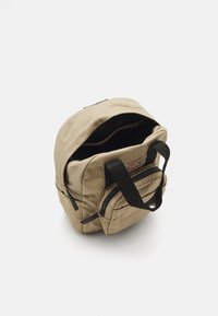 Kreemi värvi seljakott, millel on pealmine sang, kaks esimest tõmblukuga taskut ja mustad rihmad. Veidi lõtv disain, millel on õmblusdetailid.