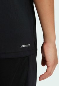 Čierne atletické tričko s textúrovanou látkou a bielym logom "AEROREADY" na leme. Tričko je skombinované s čiernymi šortkami.