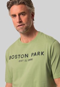Camiseta de algodón verde claro con escote redondo y mangas cortas. Texto bordado en negro que dice "BOSTON PARK EST 1996."