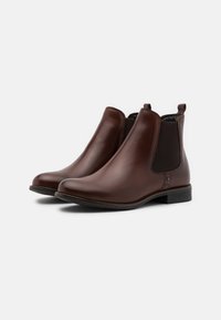 Bottes Chelsea en cuir marron avec panneaux latéraux élastiques, bout arrondi et petit talon carré. Présentent une texture lisse et une couture minimale.