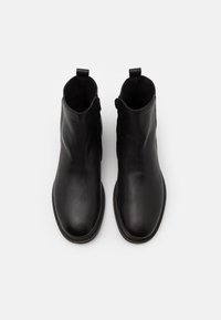 Botas de tobillo de cuero negro con una textura suave, punta redondeada, lengüetas en el cuello y detalles de costura a lo largo de la suela.