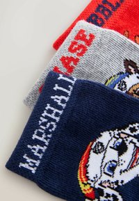 Three pairs of knitted socks in red, grey, and navy. The grey pair features red text; the navy pair has a character design and white text.