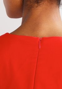 Escote de vestido rojo con una cremallera oculta en la parte posterior, con una textura suave y un diseño simple y limpio.