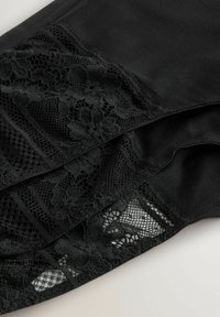 Vêtement noir avec des panneaux en dentelle texturée à motifs floraux et des détails en mesh. Tissu lisse avec des zippers aux bords inférieurs.