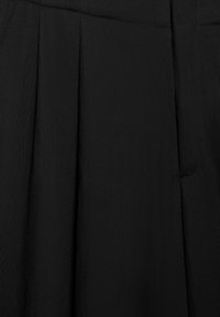 Tissu noir plissé avec des plis verticaux visibles et une couture de ceinture, suggérant un détail de jupe ou de pantalon.