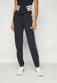 Μαύρο αθλητικό παντελόνι με λευκές πλευρικές ρίγες, ρυθμιζόμενη μέση με κορδόνι και μαλακή υφή, σε συνδυασμό με ένα ταιριαστό μαύρο μπλουζάκι.