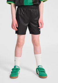 Svarta, rutiga atletiska shorts med elastisk midja, kombinerade med gröna sneakers och vita strumpor med en logotyp.
