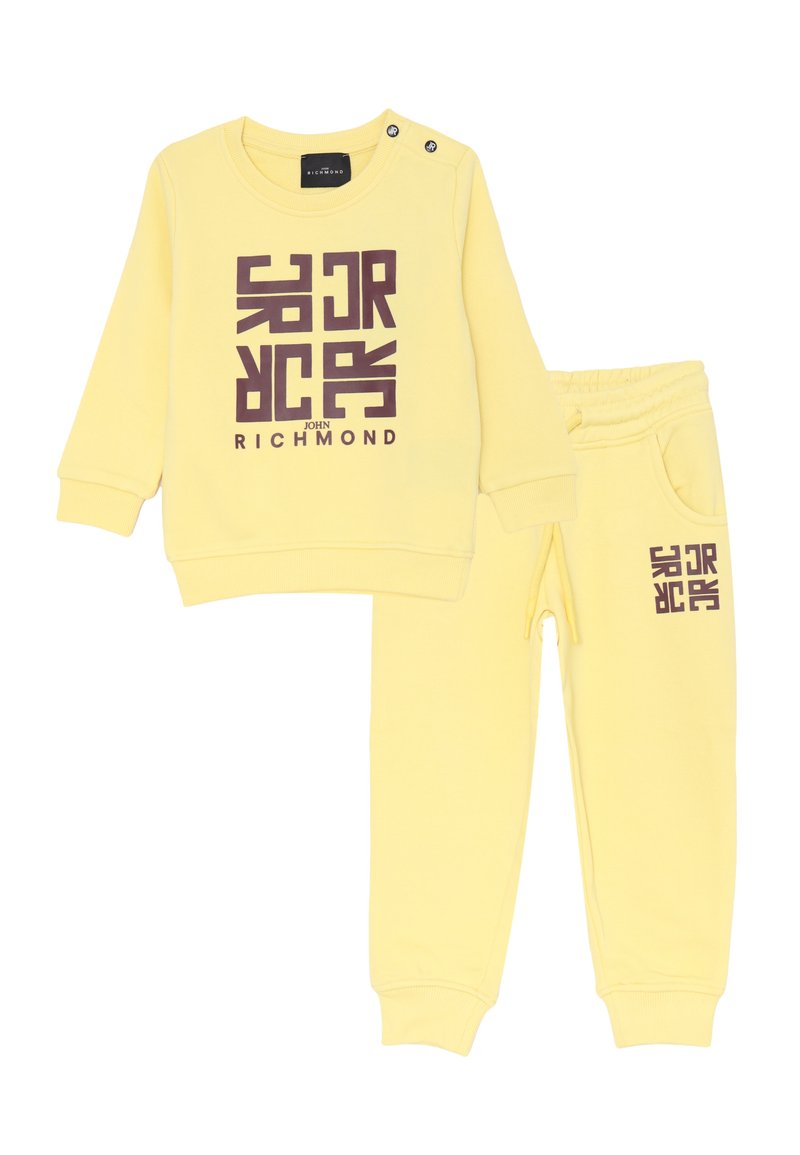 Completo felpa a maniche lunghe e pantaloni giallo per bambini con logo astratto marrone e testo "John Richmond" sul davanti e sulla gamba dei pantaloni.